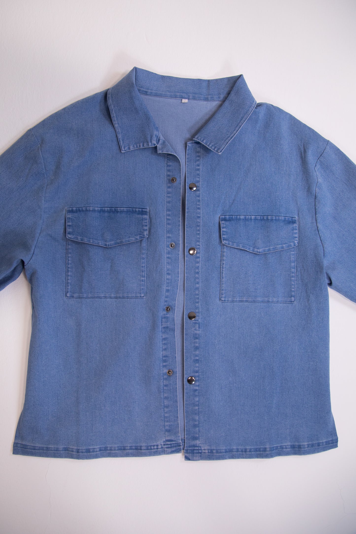 Blue denim shirt with two front pockets on a white background