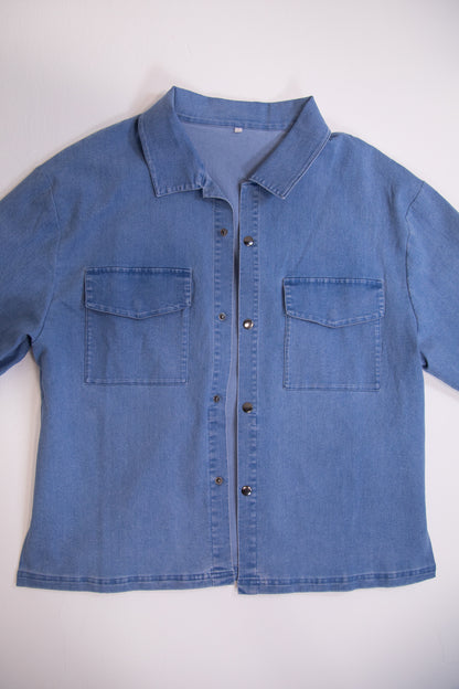 Blue denim shirt with two front pockets on a white background